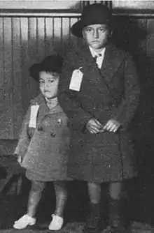 Two small boys, Campbell and his younger brother, wearing coats and with luggage tags affixed to their chests to show their destination.
