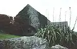 a stone building with a water wheel, rocks and plants in the foreground