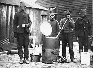 Cooking in a labour camp, Western Front, during World War I. This photograph shows four men cooking and drinking soup from one of the army outside catering boilers. They are all probably members of (4687898545)