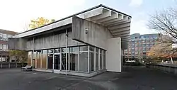 A concrete structure with an overhanging roof and large glass windows. The interior appears to be empty, with no equipment or lights.