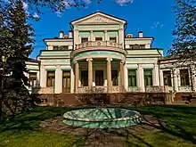 three story modern beige office building, gray portico with writing, trees, natural setting