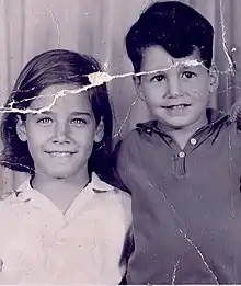 Black and white photo of a young girl seated, and a young boy standing behind her