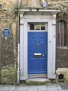 A blue door in a stone wall; a blue plaque is next to the door. This reads "Dorothy L Sayers Writer and scholar was born here 13th June 1893"