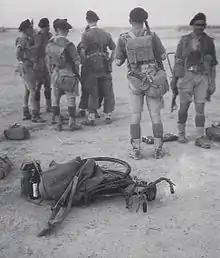 Seven British soldiers only one facing the camera, wearing hot climate uniform in a desert terrain