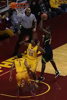 Player shooting a layup, guarded by two opponents