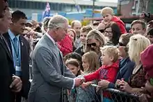 Prince Charles shakes hands with a small child in a crowd