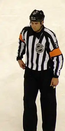 A man wearing a striped shirt with orange armbands, on the ice during a hockey game