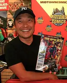 An Asian man in a black hat and T-shirt poses with a comic book.