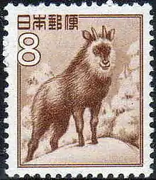 A postage stamp featuring a sepia illustration of a goat-antelope standing on a snow-covered, forested hilltop. Stylized Japanese writing in the top left corner reads: "日本郵便". Immediately below this writing is a large "8".