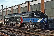 A black diesel locomotive with the Amtrak "pointless arrow" logo on the side. The blue stripes of the logo wrap around the front, where they are checked with white.