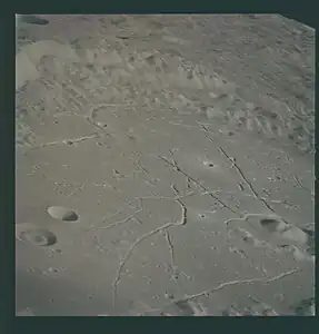 Eastern crater floor. The mare-type material on the floor contains radial cracks and concentric rilles. A dark-halo area is visible at the lower left corner. Low hills of material that resemble the central peak protrude through the smooth crater floor. Bright-halo craters are also evident. The "doughnut" filling of the crater at the left margin is a rare feature.