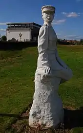 "White statue of a woman in uniform, with a chapel in the background."