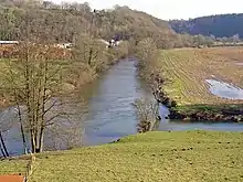 two small rivers meeting at right angles among fields and trees with some partly-obscured buildings nearby