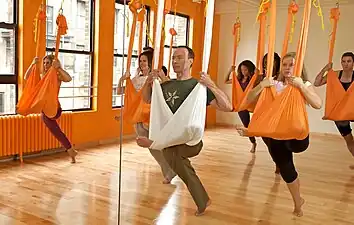 Aerial yoga class practising Flying Pigeon Pose, a hammock-supported variant