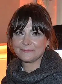 middle-aged white woman with dark hair wearing dark gray top, smiling at camera