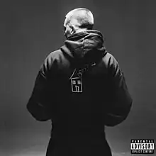 A black-and-white photo of Aitch standing away from the camera, he is wearing a hooded sweatshirt with a crude drawing of a house on it