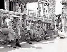  A line of six black American soldiers in service uniform (non-combat) sitting or standing beside the railing at the entrance of a temple. All are taking off their shoes prior to entering the temple.