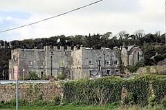 grey stone partly castellated two or three story ancient building with woods beyond