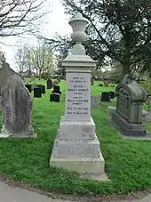 Funerary stone monument consisting of a pedestal stack of square blocks, each narrower than the one below it, upon which rests a tall, narrow cuboid with inscriptions, above which is a square capitol topped with a carved urn