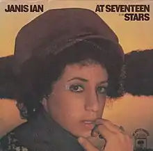 An image of a woman showing her teeth with a finger on her lips while looking to the camera. She has large, curly hair. The words "Janis Ian", "At Seventeen" and "Stars" are placed over the image in the same font and black color. Words about the record company are also included.