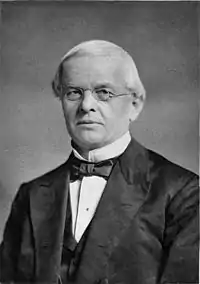 Head and torso portrait in black and white.  Depicts a light-haired man in dinner jacket and bow tie, wearing thin wire-rimmed spectacles.