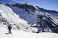 Avalanche Team skier on Haystack Butte summit, with Garden Wall, Bishops Cap, and Pollock Mountain in the background.