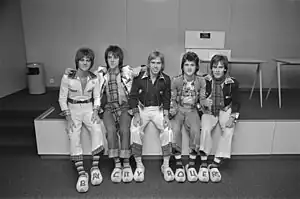 Five young men, two in tartan shirts, all wearing Dutch clogs