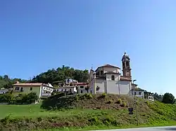 Buildings with red roofs sit on a green hill. One of the buildings is the church of the Natività di Maria and has a red belltower.