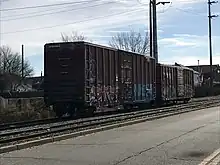 Two boxcars on a siding, adjacent to a second track and then a roadway.