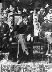 Masaryk, seated with his legs crossed and saluting the photographer