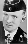 A black-and-white photograph of a man wearing a military uniform, side cap and a neck order in shape of an Iron Cross.