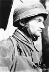 A man wearing a camouflage military uniform and steel helmet.