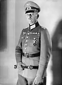 A man wearing a military uniform and peaked cap holding a baton.