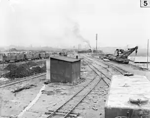 This 1917 photo of the military rail transport at Ypres shows a water tank wagon in the right foreground. Behind the tank wagon is a partially armoured, 16-wheel, hand-operated light railway crane capable of lifting 6 long tons (6.7 short tons; 6.1 t). The crane was built by Ransomes & Rapier of Ipswich, Suffolk. Cars in the left background appear to be loaded with crates of food or ammunition.