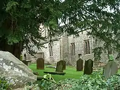 Side of stone building with arched windows, partially obscured by trees. Gravestones in the foreground