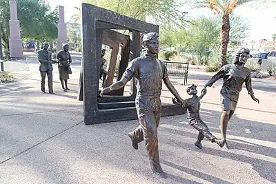 Life-size metal statues of people look like they have just joyfully emerged from a series of abstract door frames representing cancer as a journey