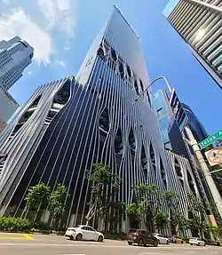 Ground-level view of a 50-storey building, distinct architecture features modern hole designs with trees in them.