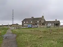 Inn building behind vehicles in car park, with nearby mobile phone tower to rear