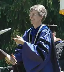 A woman in purple academic regalia passes a diploma to a student, out of frame.