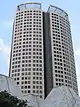 Ground-level view of a 40-storey skyscraper with a rounded facade and an open, lattice-work structure on the roof