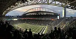 A stadium filled with spectators with two football teams on the field between a play.