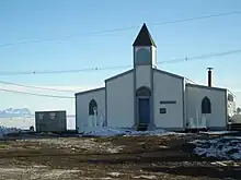 A low slung white and blue clapboard building with a single central steeple.