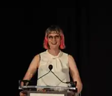 Photo of a purple haired woman standing at a podium