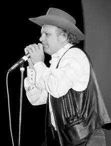 Charlie McCoy, wearing a stetson hat, at a microphone