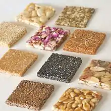 Ten flat squares of chikki. The different colors and textures are due to each square being made from a different type of nut or seed.