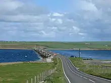 The causeway, made from many concrete blocks, carries a road between the islands. The sea is rough on one side of the barrier but calm on the other.