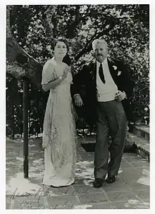 Dr. Logan Clendening stands to the left of his wife, Dorothy Hixon Clendening. He leans on the edge of an invisible object. He is wearing a suit. Dorothy is wearing a white dress and holds a cigarette.