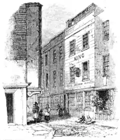 A monochrome illustration of a narrow street, viewed from a corner, or intersection. A large three-storey building is visible on the right of the image. The ground floor has three windows, the first and second floors have two windows each. The roof appears to contain a row of windows, for a loft space. The word "KING" is written between the first and second floors, and a sign, "Gas meter maker" hangs above the ground floor windows.