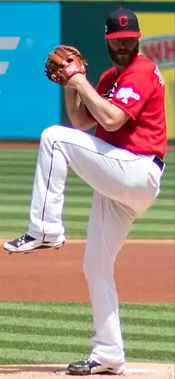 A baseball player in a red jersey and white pants in his wind-up preparing to pitch a ball from the mound