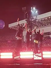 Four men holding each other's hands raise their arms to thank their audience